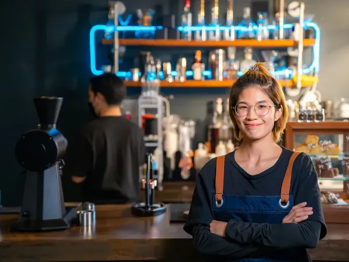 Confident small business owner standing behind the counter in her café representing community entrepreneurs featured on Town Service Connect Now